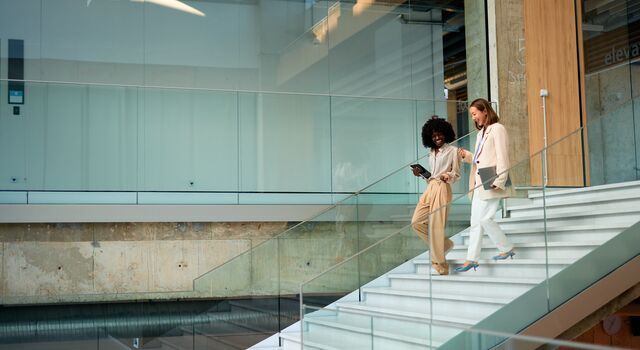 COLOUR-IMAGE_buisness women-walking-through-modern-office-building-holding-laptops_jul26