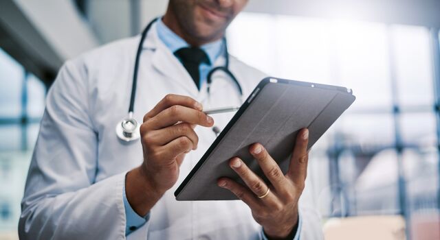 COLOUR-IMAGE_male-doctor-smiling-at-tablet-screen_apr26
